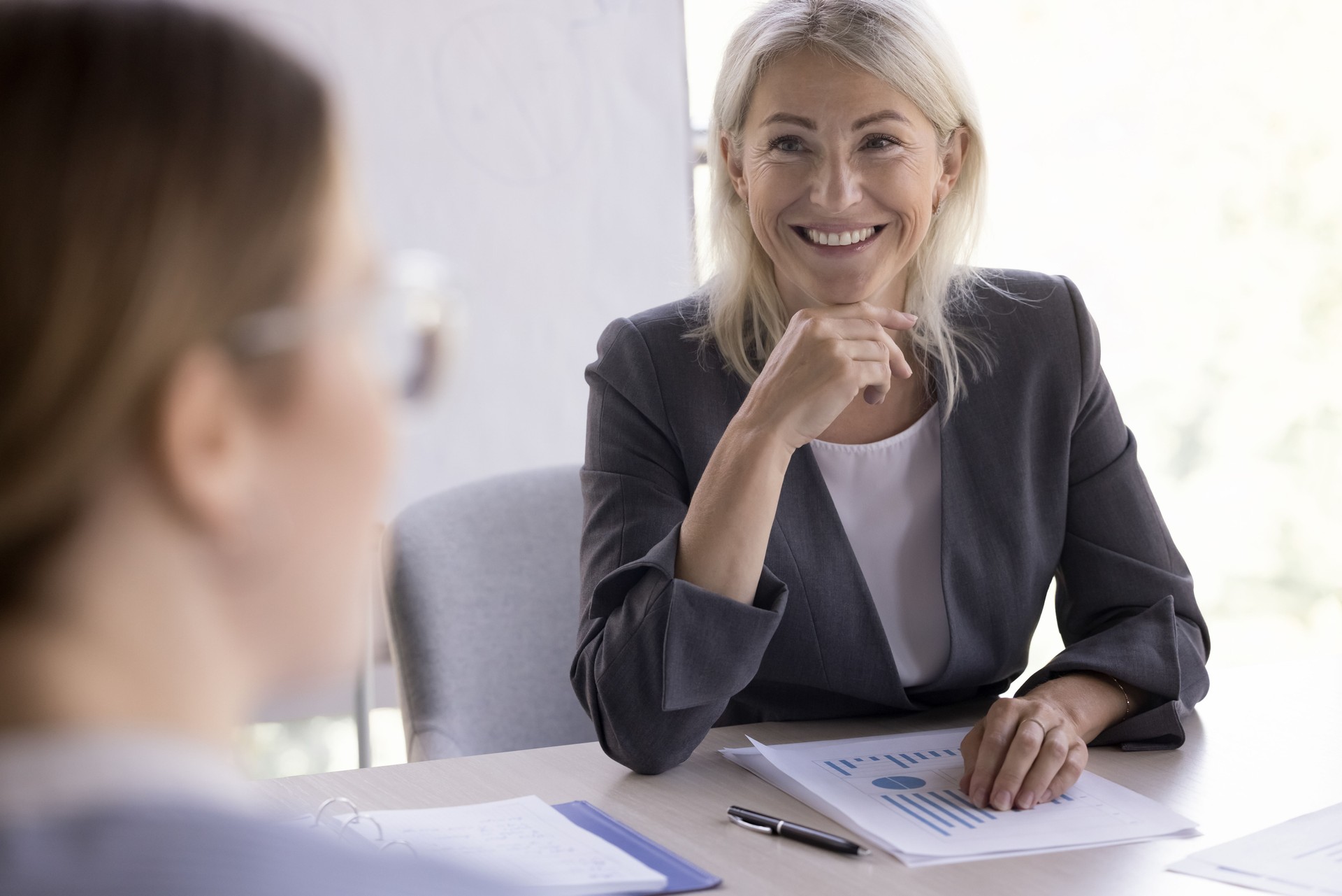 Cheerful confident mature businesswoman talking to partners on negotiation meeting